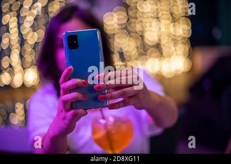 Woman using smartphone indoors with glowing lights in background Stock Photo
