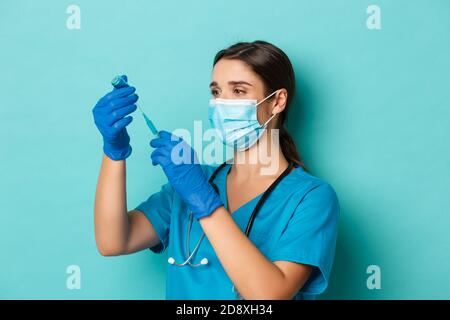 Concept of covid-19 and quarantine concept. Image of female doctor in medical mask, gloves and scrubs, filling syringe with coronavirus vaccine Stock Photo