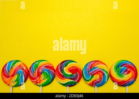 Bright swirl lollipops on yellow background with copy space. Festive background with colorful twisted candies. Stock Photo