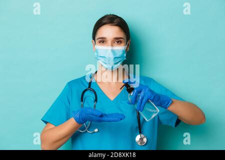 Concept of covid-19 and quarantine concept. Close-up of beautiful female doctor in medical mask, gloves and scrubs, using hand sanitizer, standing Stock Photo