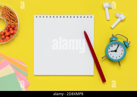 Notebook and pen on a yellow background. Notepad, white headphones, alarm clock, clips, and colorful stickers on workplace. Template with copy space, Stock Photo
