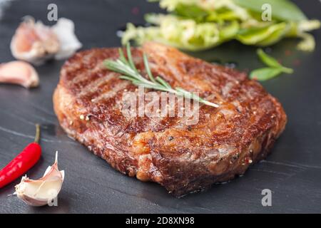 A juicy rib-eye on a black stone table with garlic and chilli Stock Photo