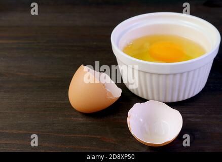 Closeup cracked eggshell on dark brown wooden table with blurry raw egg bowl in background Stock Photo