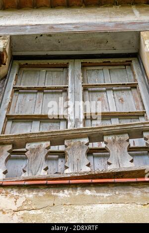 cracked ruin with a damaged window with closed wooden shutters and a cracked wall. Dilapidated house for demolition Stock Photo