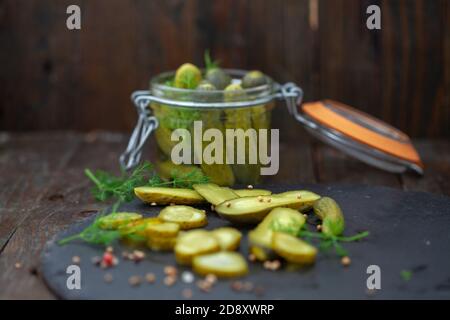 Pickled cucumbers with herbs and spices on wooden background. Homemade marinated cornichons in a jar. Stock Photo