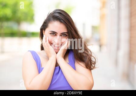 Happy young woman hands on face looking at camera outdoors Stock Photo