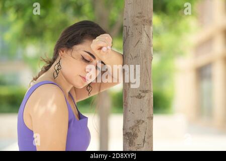 Sad woman leaning against tree Stock Photo