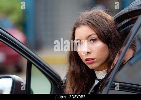 young, smiling woman  sits in a car with an open door and looks back, close-up portrait Stock Photo