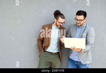 Positive successful business specialists discussing plan with laptop outdoors. Stock Photo