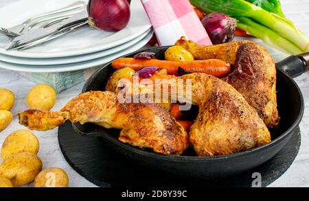 Meal with roasted chicken legs served for dinner in an skillet on a table with plates Stock Photo