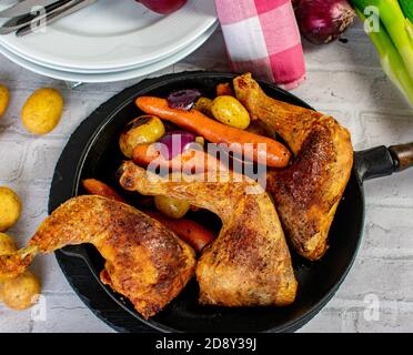 roasted chicken legs with oven baked vegetables served in a rustic iron pan on a table from above view Stock Photo