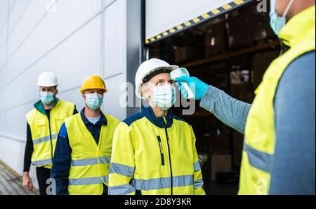 Group of workers with face mask in front of warehouse, coronavirus and temperature measuring concept. Stock Photo