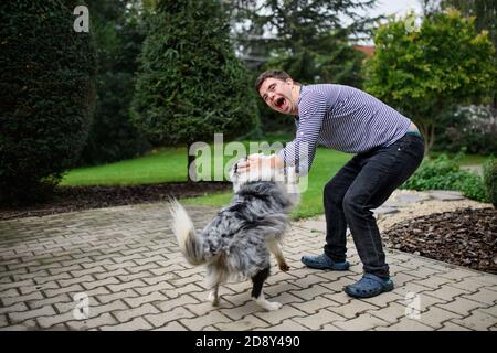 Portrait of cheerful down syndrome adult man playing with dog outdoors in backyard. Stock Photo