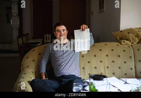 Down syndrome adult man sitting indoors at home, writing. Stock Photo