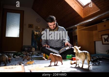 Down syndrome adult man sitting indoors in bedroom at home, studying about animals. Stock Photo