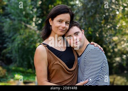 Portrait of down syndrome adult man with mother standing outdoors in garden. Stock Photo