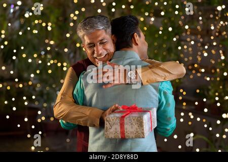 A SENIOR ADULT MAN HAPPILY HUGGING SON WITH GIFT IN HAND Stock Photo