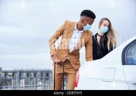 Business Couple Wearing Masks Outside Airport Getting Luggage Out Of Car During Health Pandemic Stock Photo
