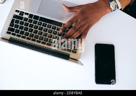 Overhead Shot Of Businessman Working On Laptop At Hot Desk In Office With Mobile Phone Stock Photo