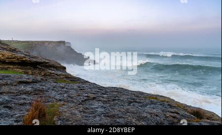 huge storm waves crash onto the Cape Ajo in Spain with the lighthouse on the cliffs above at sunrise Stock Photo