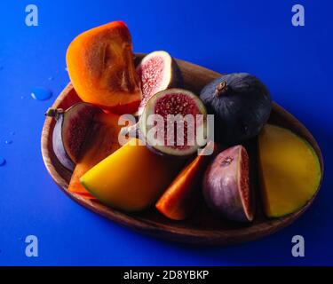 Persimmon, figs and mango sliced on a wood platter top view on blue Stock Photo