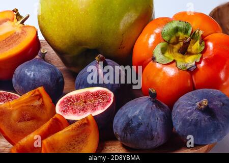 Portion of sliced figs, apple, persimmon  and mango on a wood platter on white Stock Photo