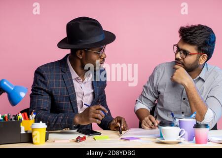 Closeup shot of african american businessman and indian enterpreneur discussing business plans, sitting at table in office, wearing formal wear, smili Stock Photo