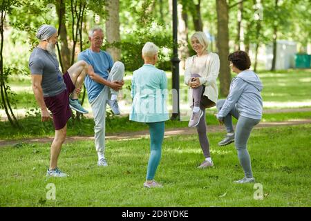 Group of modern senior people spending sunny morning in park doing stretching exercise Stock Photo