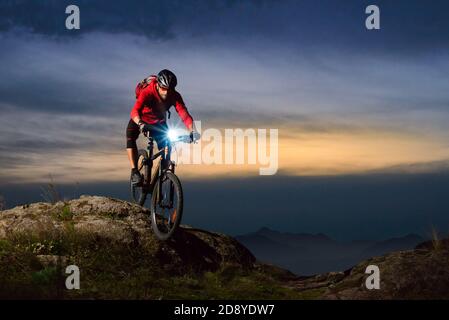 Cyclist Riding the Mountain Bike on Rocky Trail at Night. Extreme Sport and Enduro Biking Concept. Stock Photo