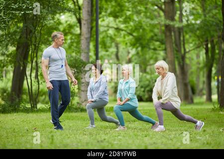 Wide shot of three good-looking senior women having workout in city park with trainer looking at them Stock Photo