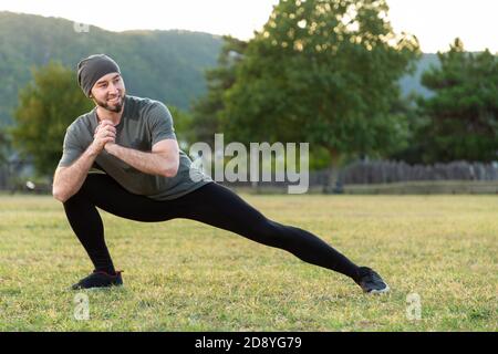 Sports and yoga. A man with a beard, in sportswear performs stretching on the grass before training. Stock Photo