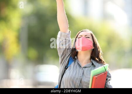 Front view portrait of an excited student wearing mask raising arm in the street celebrating success Stock Photo