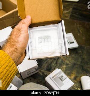 Paris, France - Oct 25, 2020: Man hand holding unboxing new Vaillant Ambisense VR51 room thermostat connected IoT device to the gas heating pump boiler - covered with paper Stock Photo