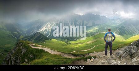 Hiker Man standing in deep hanging clouds above mountains and valley. Mystic light breaks through fog. Tirol, Austria. Stock Photo