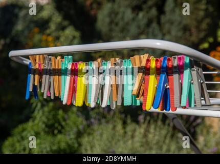 A colored clothes pegs hanging on a drying rack wire. A group of clothespin in line on stand at the sunny garden. Stock Photo