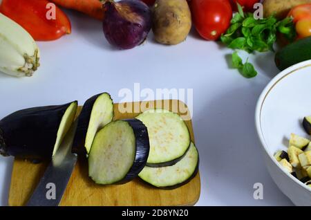 Female hand with knife cuts eggplant on board in kitchen. Cooking vegetables. to make a vegetable stew or salad. vegetarianism, diet, low calories Stock Photo