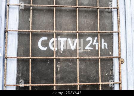 Old, forlorn boarded up property with rusty metal window bars and roughly painted CCTV 24h warning. Rough security. Urban decay Stock Photo