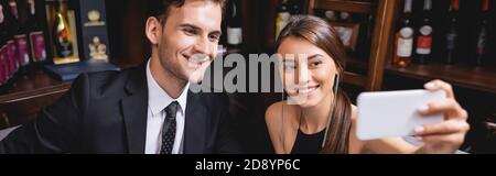 Panoramic crop of elegant couple taking selfie on smartphone in restaurant Stock Photo