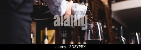 Panoramic shot of sommelier holding towel while pouring wine from decanter in restaurant Stock Photo