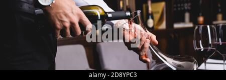 Panoramic shot of sommelier pouring wine in decanter near glasses in restaurant Stock Photo