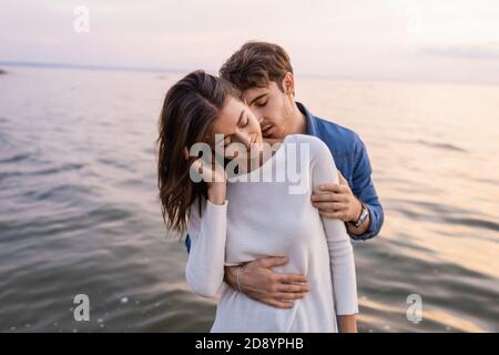 Man kissing neck and hugging girlfriend near sea at evening Stock Photo