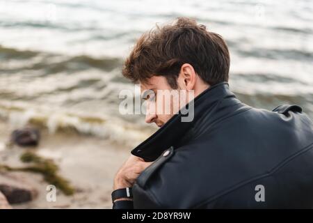 Back view of young man in black leather jacket on sea coast Stock Photo