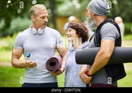 Two sporty mature men and woman standing together in park discussing something before doing exercise Stock Photo