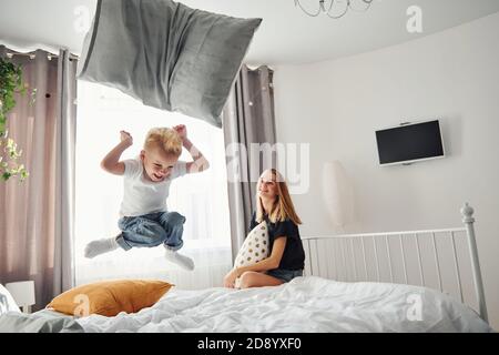 Mother playing pillow fight with her son in bedroom at daytime Stock Photo