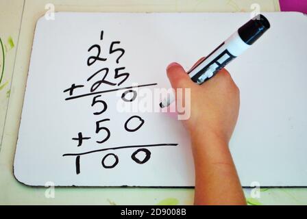 Second grade girl learning how to carry the one on a whiteboard while distance learning not common core math Stock Photo