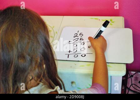 Second grade girl learning how to carry the one on a whiteboard while distance learning not common core math Stock Photo