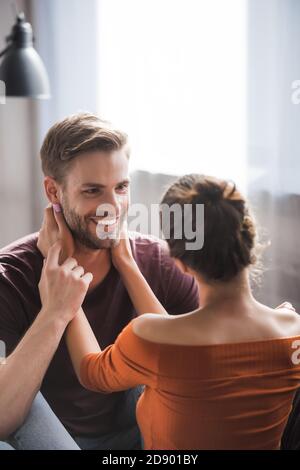 back view of young woman hugging neck of happy boyfriend while standing face to face at home Stock Photo