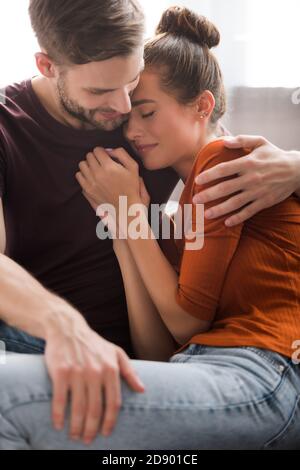 young man embracing upset girlfriend while calming her at home Stock Photo
