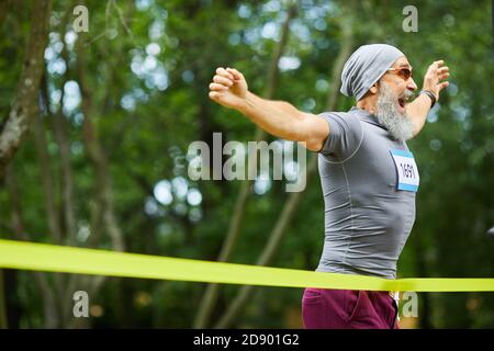 Happy bearded senior man wearing cap and sunglasses winning first place in marathon race, copy space Stock Photo