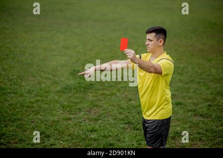 Angry football referee showing a red card and pointing with his hand on penalty Stock Photo